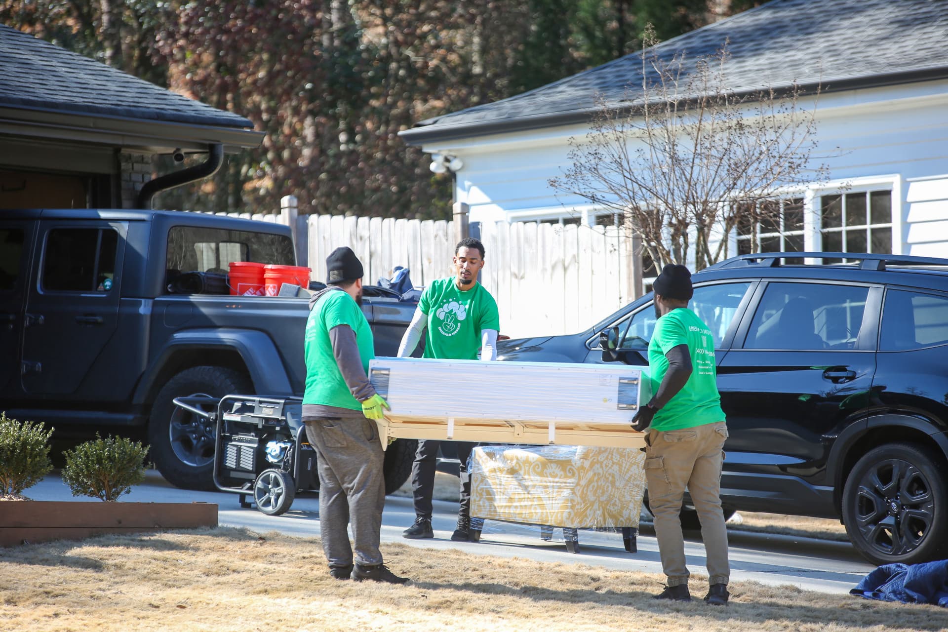 Emerald Movers crew carrying a wrapped bed frame across a Metro Atlanta driveway