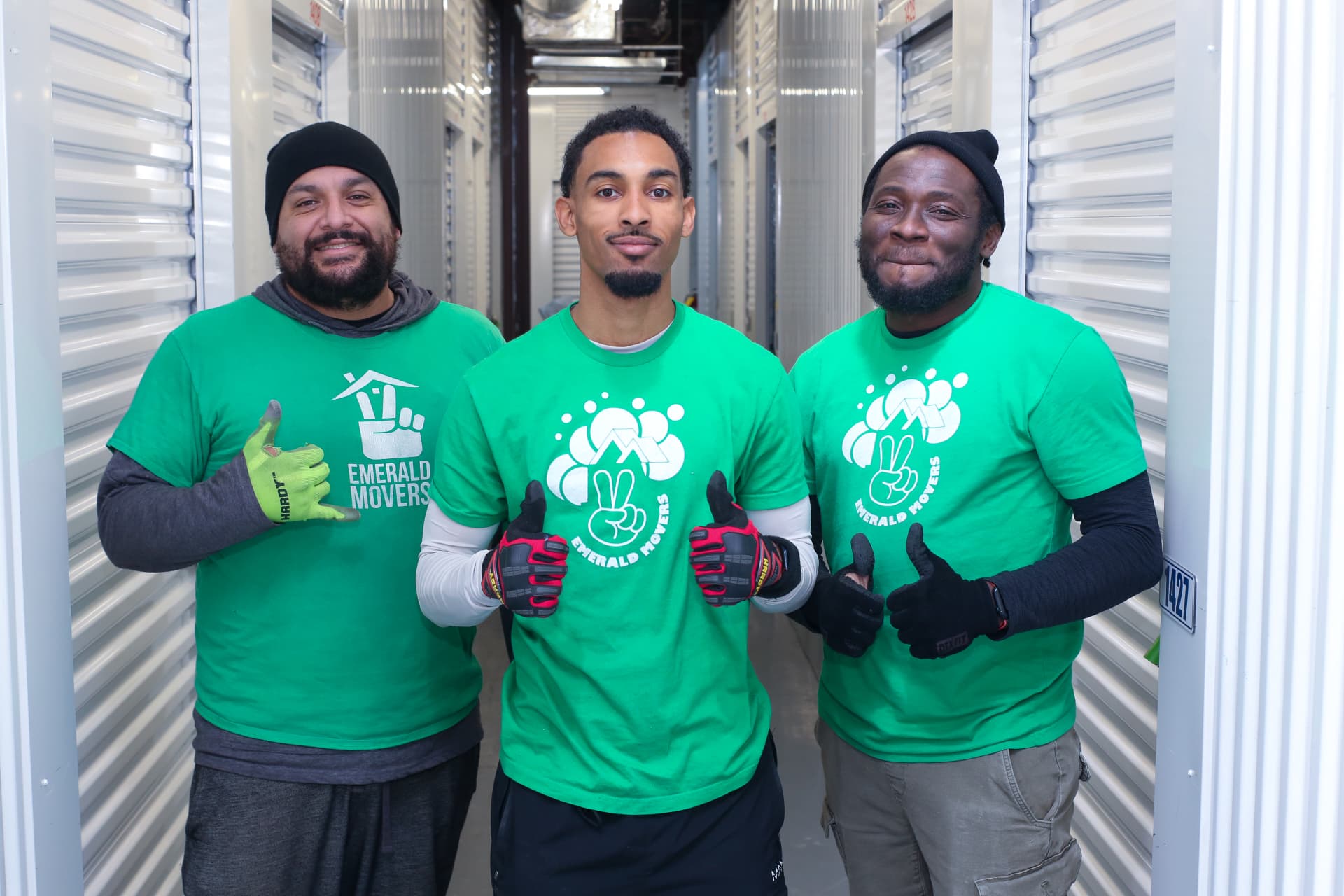 Three Emerald Movers crew members giving a thumbs up in a storage hallway